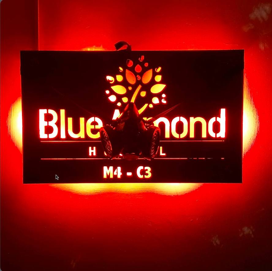 The hostel’s illuminated sign glowing red: “Blue Almond Hostel — M4 · C3”, with an almond tree logo.