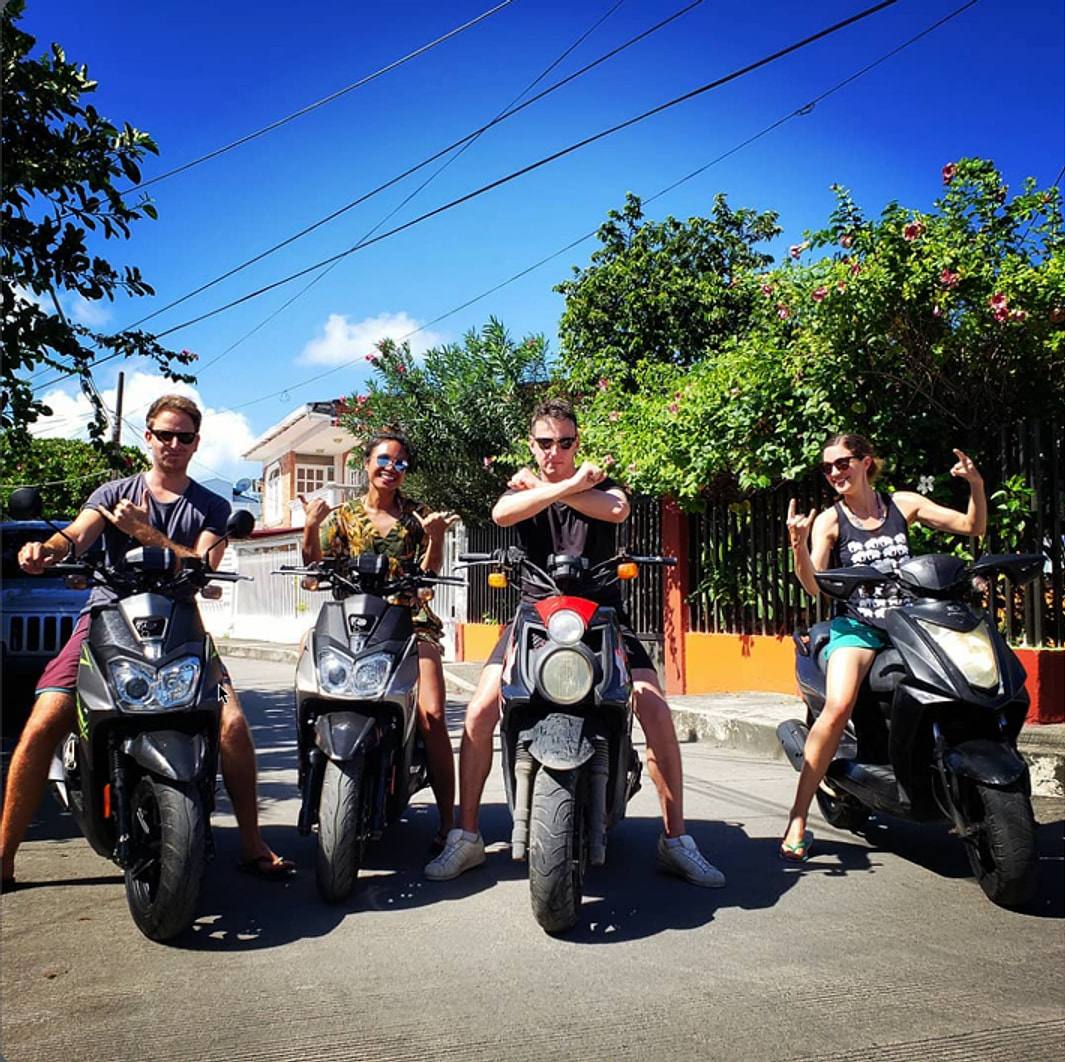 Four guests posing on rental scooters on a sunny San Andrés street.